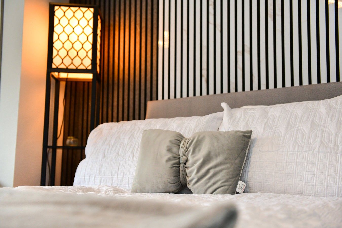 A neatly made bed with a headboard, two pillows, and a bedside lamp.