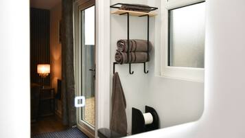 A hotel room with a door leading to a balcony, a towel rack with towels, a window, and a lamp.