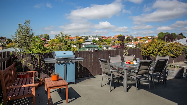 An outdoor patio with a barbecue grill, seating area, and a view of a residential neighborhood. - Homestead Lodge Motel (Timaru)