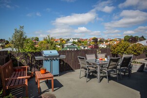 Un patio exterior con una parrilla, zona de estar y vista a un barrio residencial.