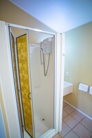 Una ducha con puerta de cristal, pared blanca y suelo de baldosas.