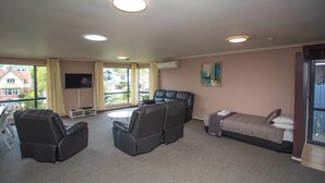 A room with a sofa, chairs, a bed, a flat-screen TV, and a window with curtains. - Homestead Lodge Motel (Timaru)