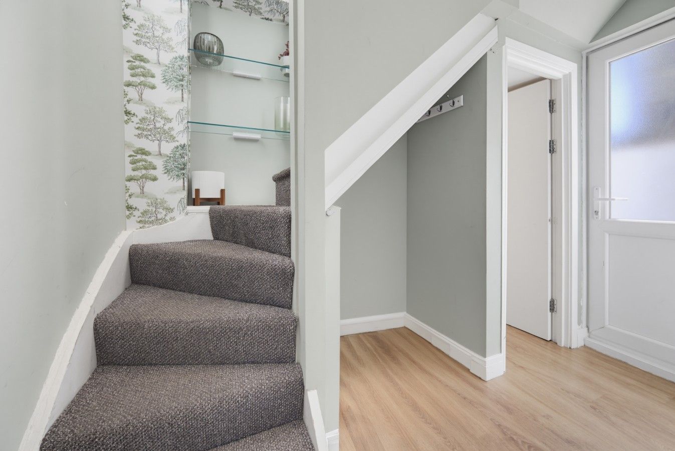 A staircase with carpeted steps leading to a room with a door and a glass shelf with decorative items.