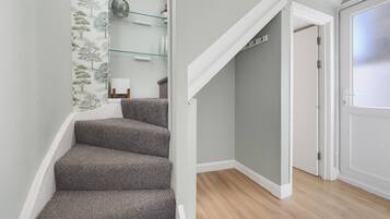 A staircase with carpeted steps leading to a room with a door and a glass shelf with decorative items.