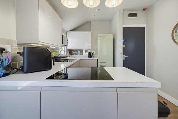 A modern kitchen with white cabinetry, a built-in stove, and a refrigerator. - Stylish Canton Retreat with Private Garden – Short Distance to Cardiff Castle & Stadiums! (Cardiff)