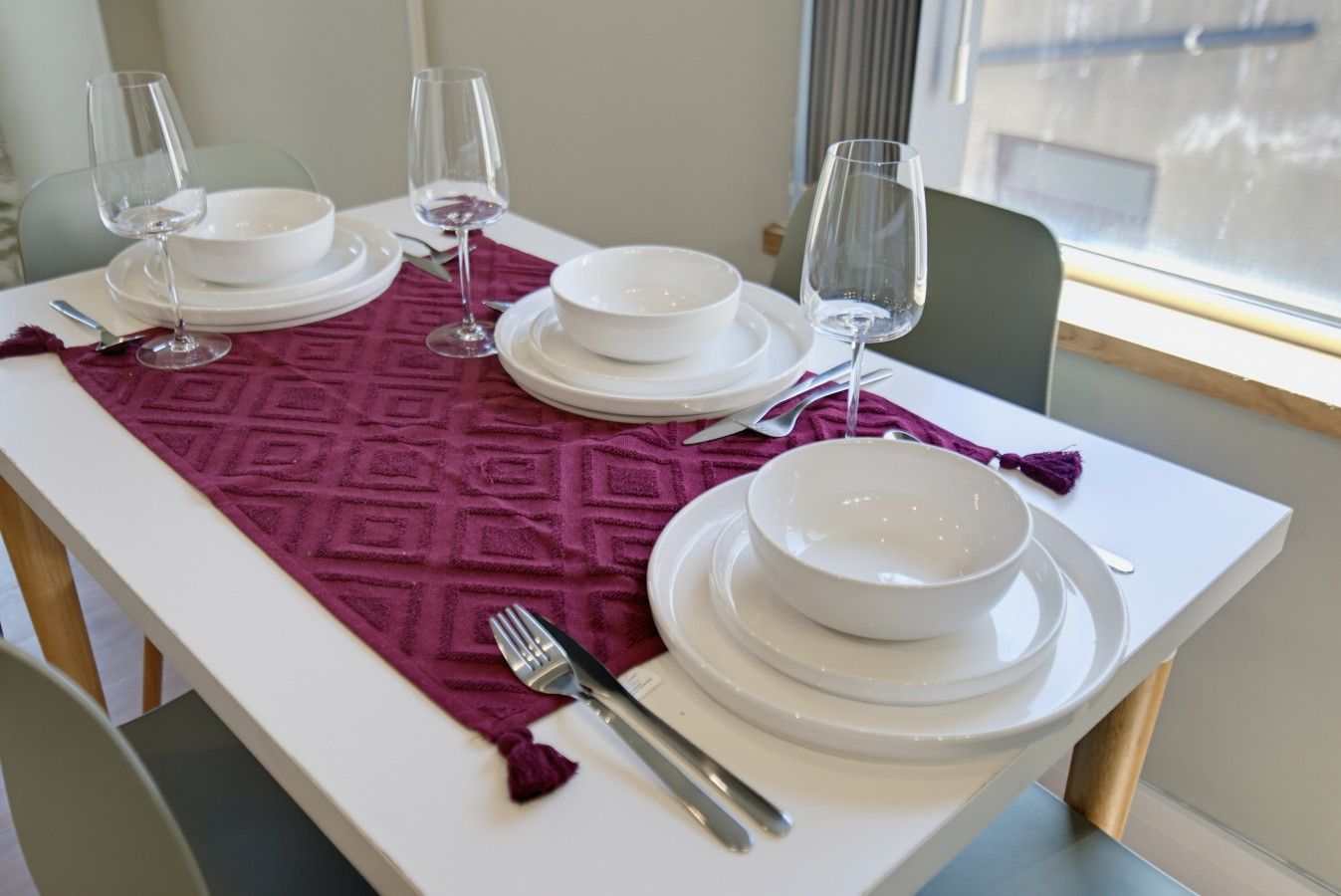 A dining table set with white plates, bowls, and wine glasses, a fork, and a patterned table runner.