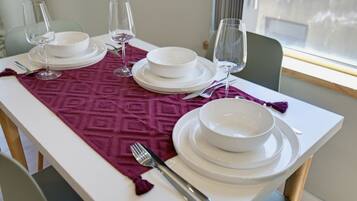 A dining table set with white plates, bowls, and wine glasses, a fork, and a patterned table runner.