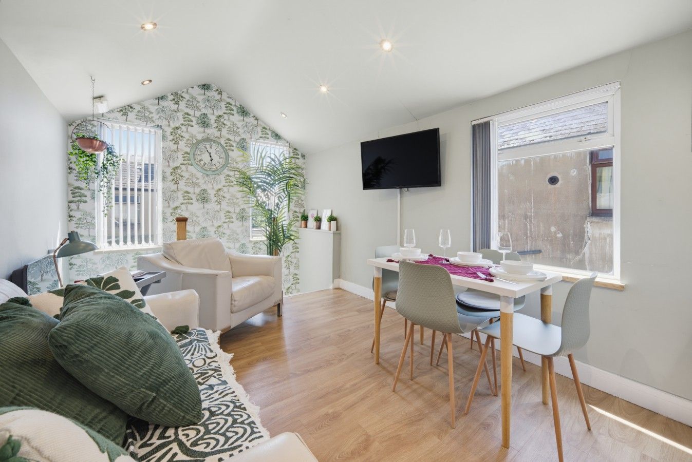 A modern living room with a dining area, wooden flooring, and a large window with blinds.