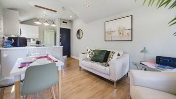 A modern living room with a white sofa, a dining table set for two, and a kitchen in the background.