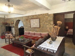 Uma sala de estar acolhedora com parede de pedra, um sofá vermelho, uma mesa de centro de madeira e um candelabro.