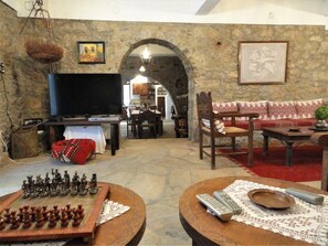 A living room with a stone wall, a television, a chessboard, and a sofa. - Zeus House (Lasithi Plateau)