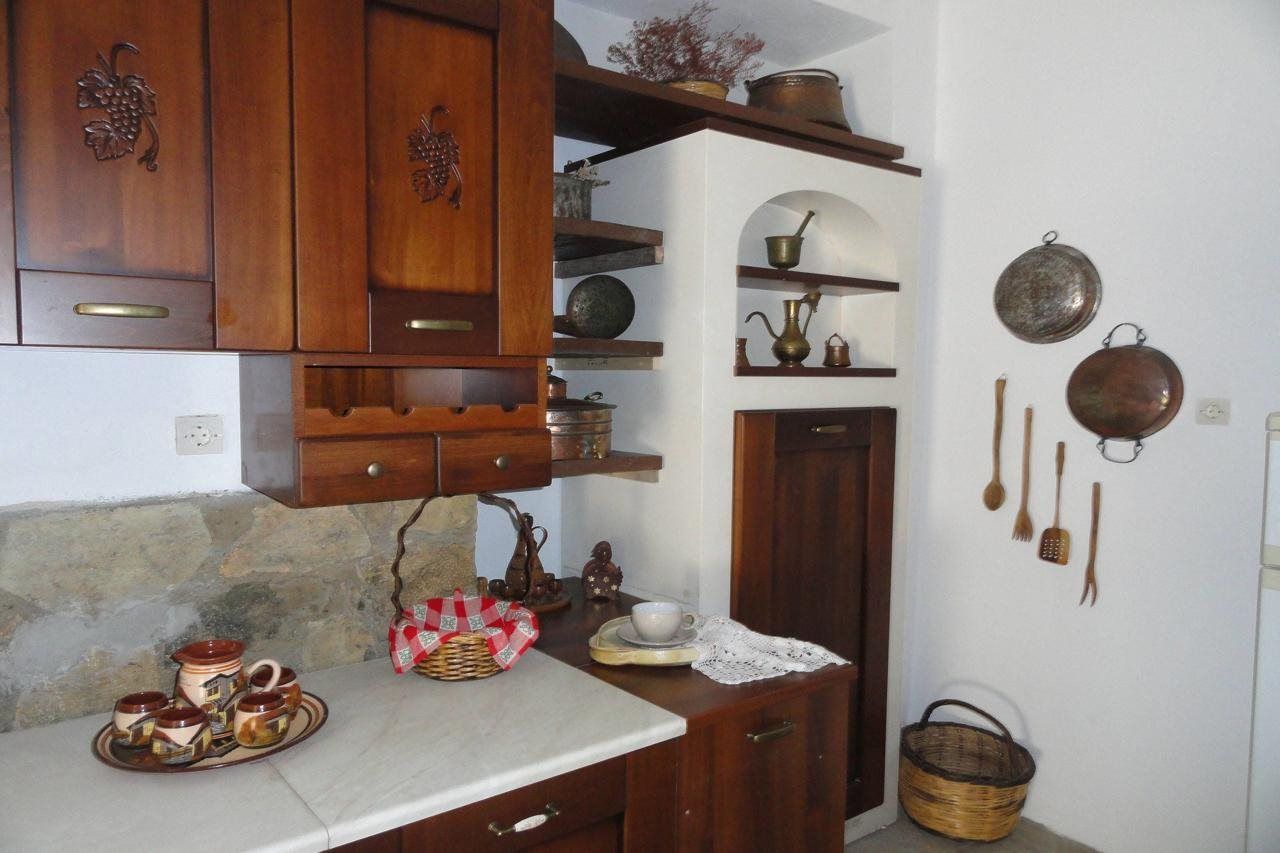 Eine Küche mit Holzausstattung, einer Steinrückwand sowie verschiedenen Küchengeräten und Kochutensilien, die in Regalen und an der Wand präsentiert werden.