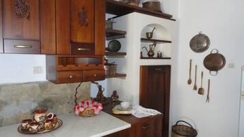 Eine Küche mit Holzausstattung, einer Steinrückwand sowie verschiedenen Küchengeräten und Kochutensilien, die in Regalen und an der Wand präsentiert werden.
