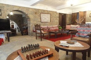 A cozy living room with a chessboard, wooden furniture, stone walls, and a television. - Zeus House (Lasithi Plateau)