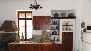 A kitchen with wooden cabinets, a built-in stove, and a hanging light fixture. - Zeus House (Lasithi Plateau)