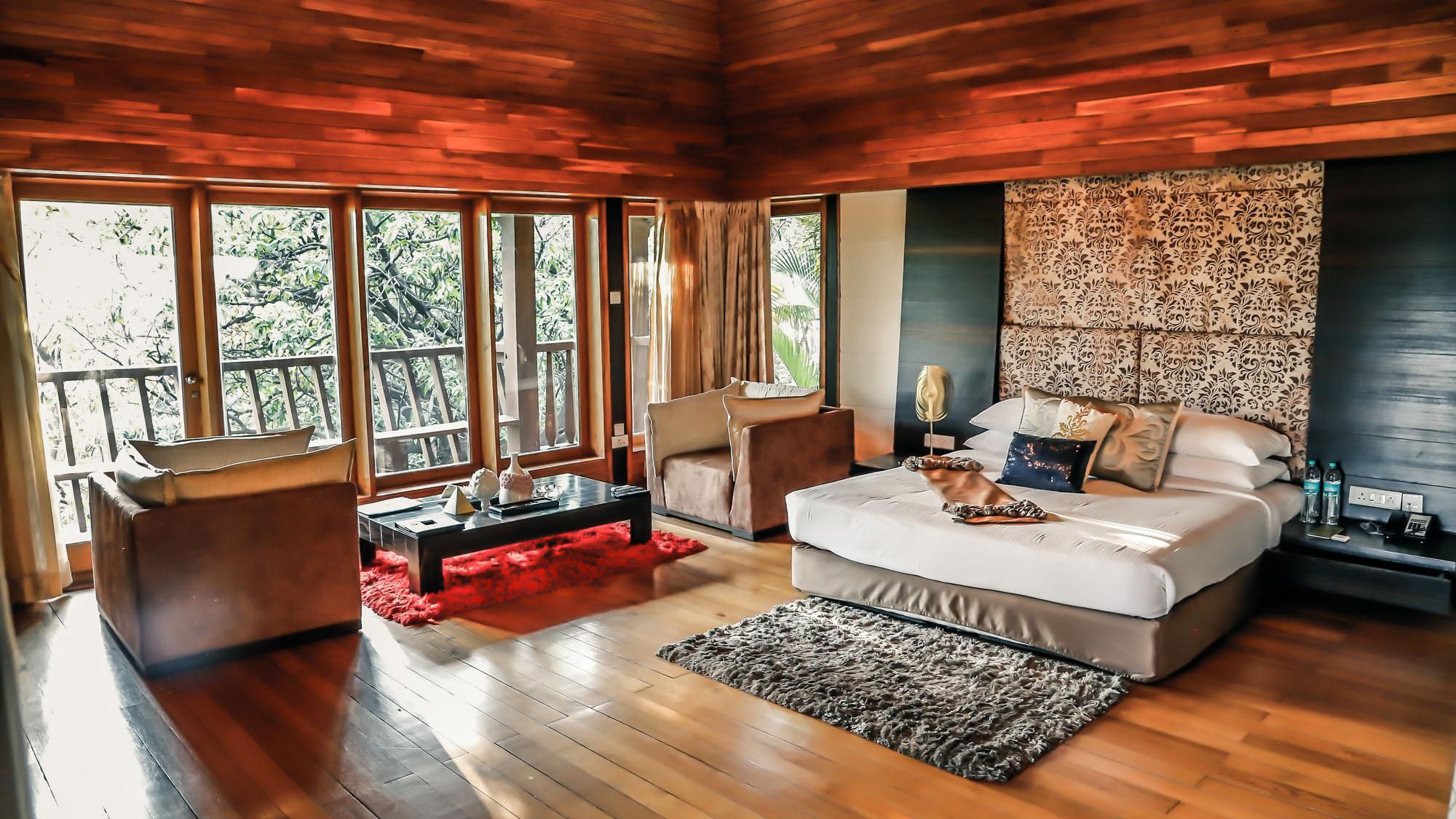 A spacious room with a large bed, a seating area, and a view through large windows.
