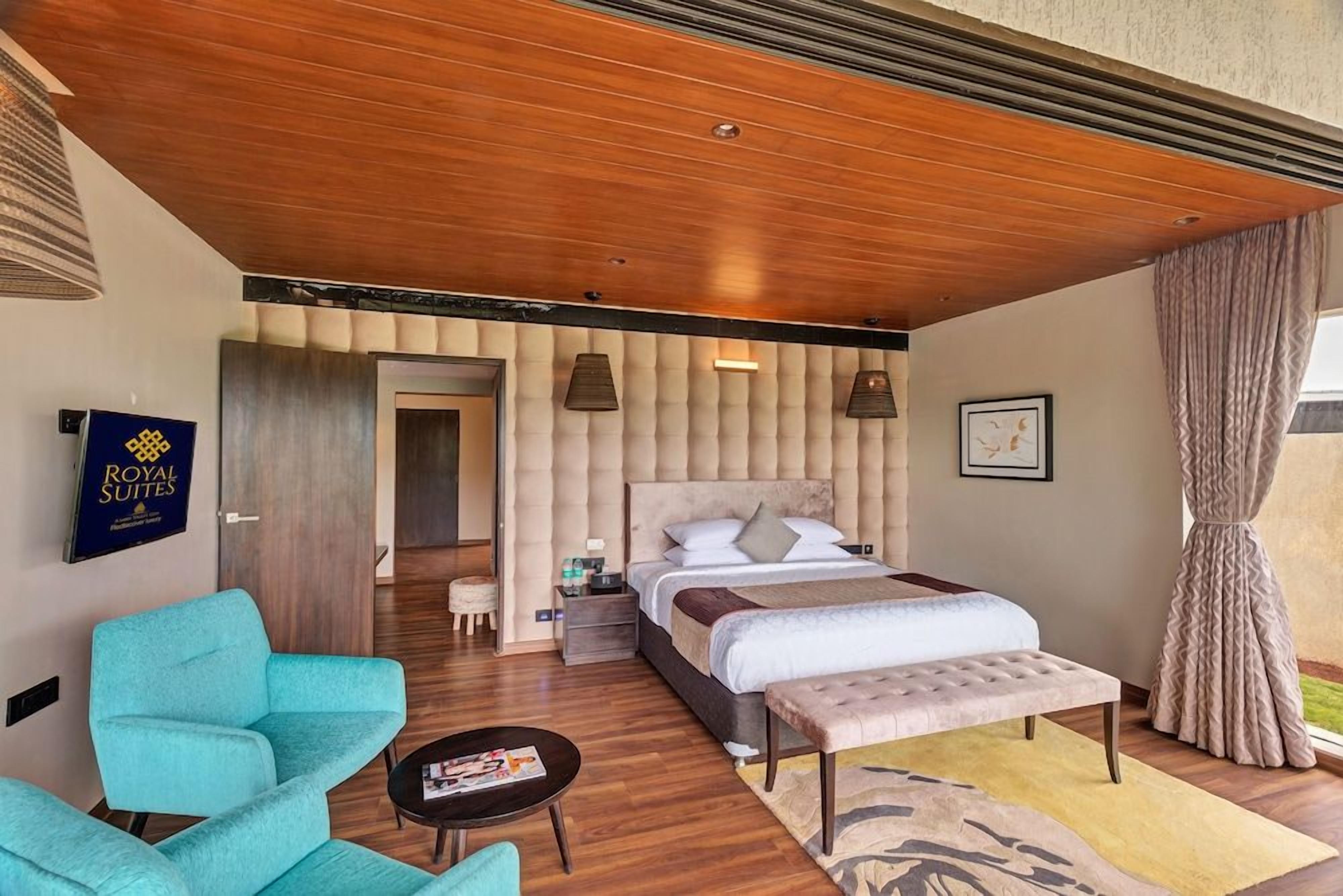 Une chambre d’hôtel comprenant un lit, un coin salon avec un fauteuil, une petite table et une fenêtre avec des rideaux.