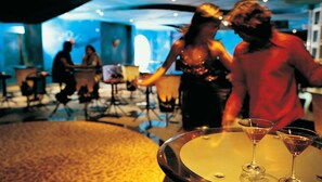 A bar area with round tables and martini glasses, a person in a red shirt, and a woman in a black dress. - Aamby Valley City, Lonavala (Paud)