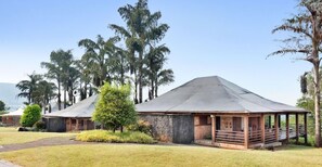 A building with a sloped roof, surrounded by trees and a grassy area. - Aamby Valley City, Lonavala (Paud)