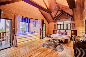 A spacious room with a large bed, a seating area, and a view through a glass door. - Aamby Valley City, Lonavala (Paud)