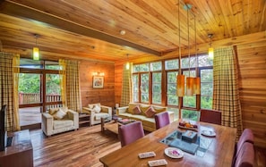 A wooden cabin interior with a dining table, sofas, and large windows. - Aamby Valley City, Lonavala (Paud)