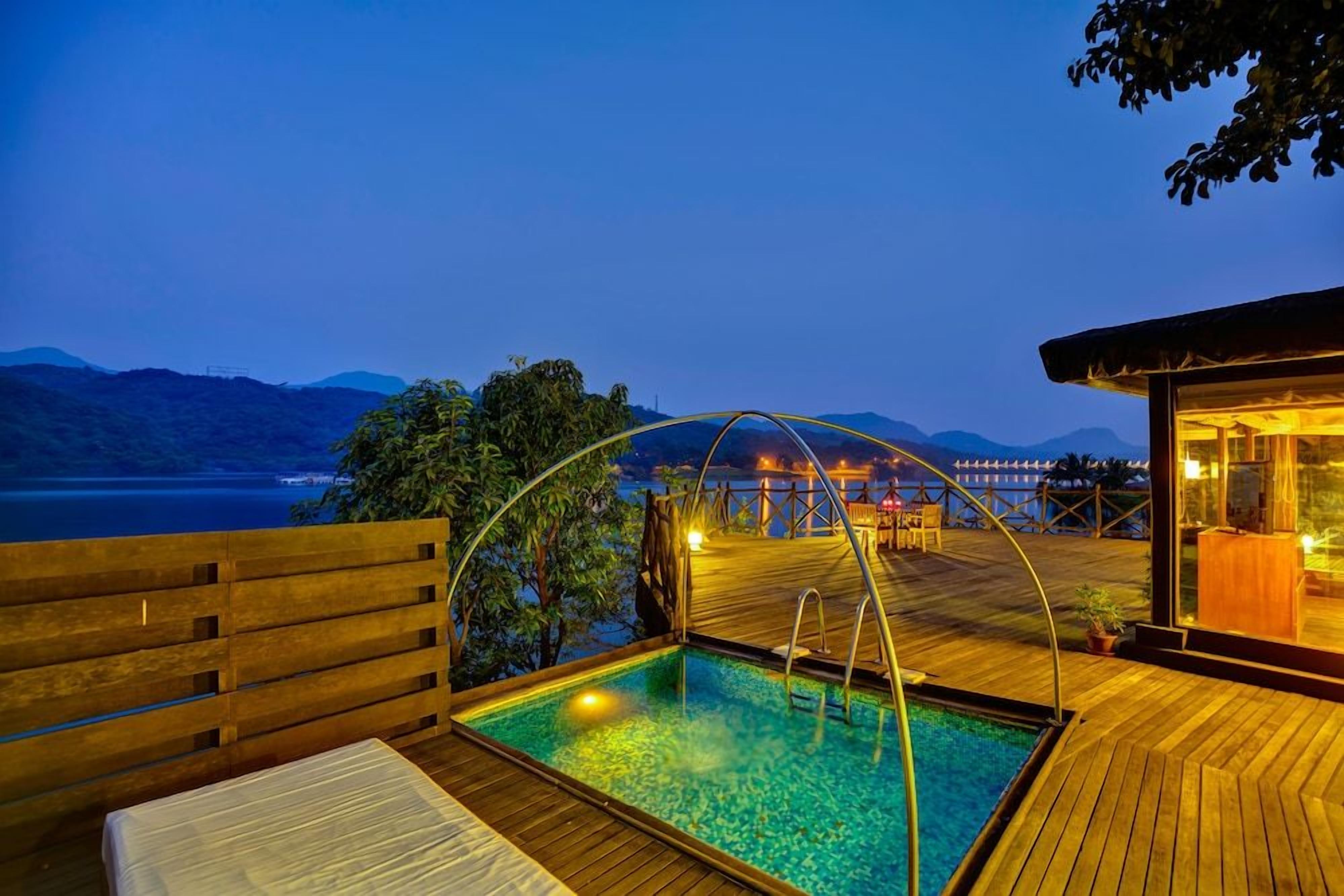 A wooden deck with a pool, overlooking a body of water and mountains.