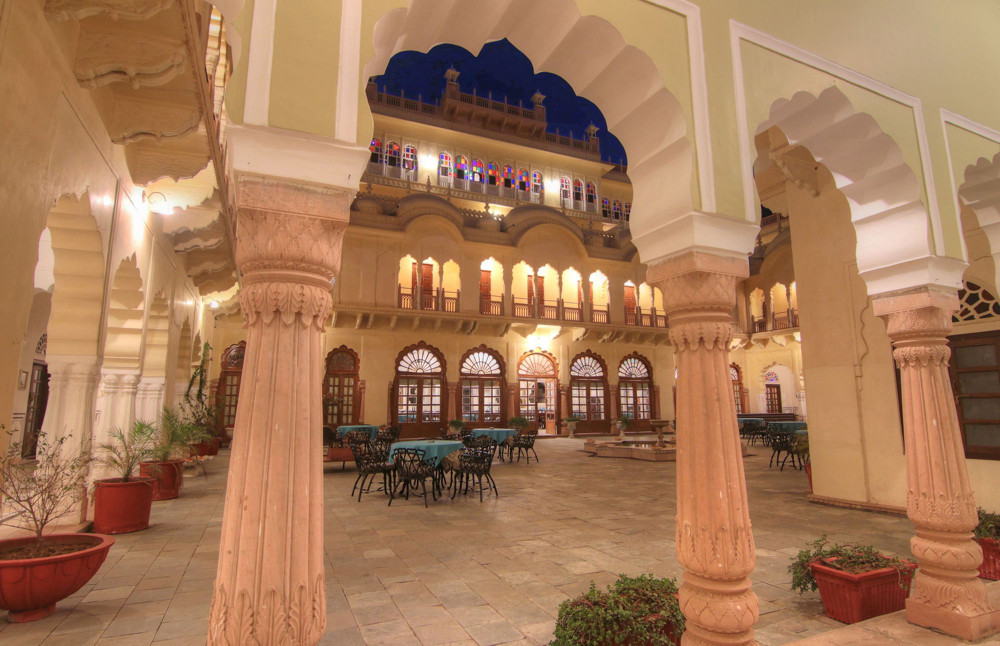 An indoor courtyard with ornate columns, a balcony with colorful window patterns, and a tiled floor.