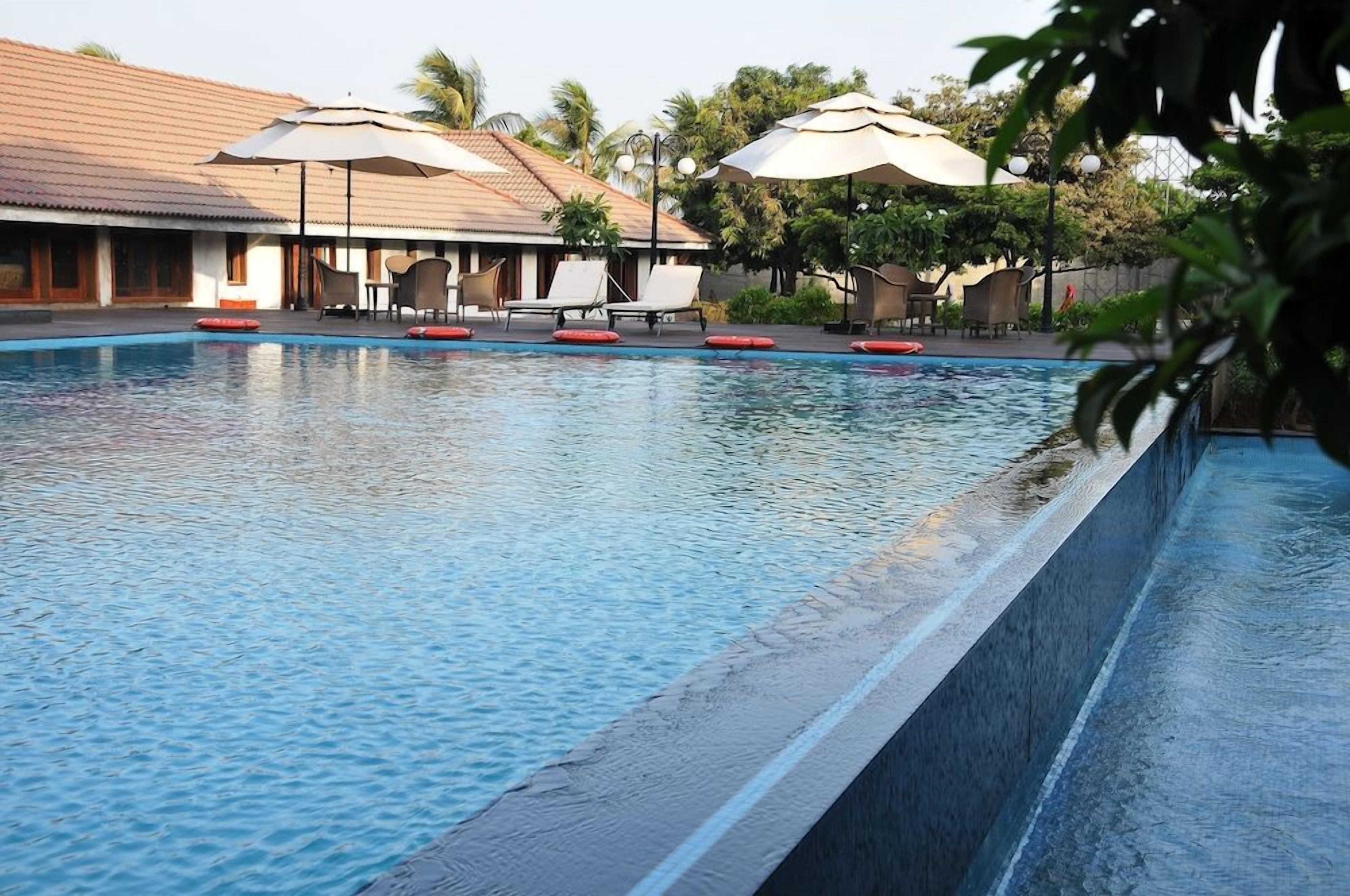 A swimming pool with lounge chairs and umbrellas, surrounded by a building with a tiled roof.