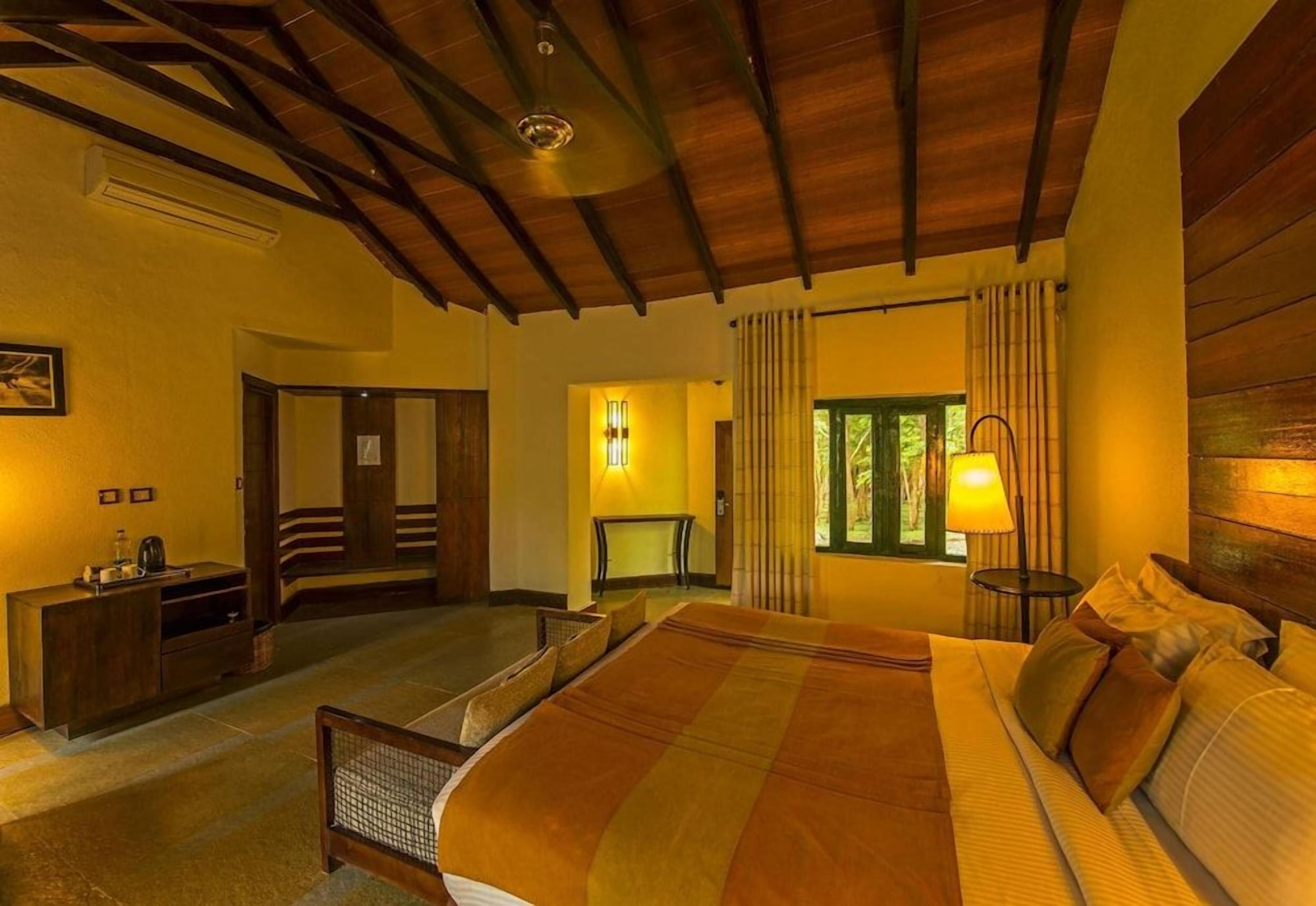 A hotel room with a large bed, a desk, a chair, a window with curtains, and a ceiling fan.