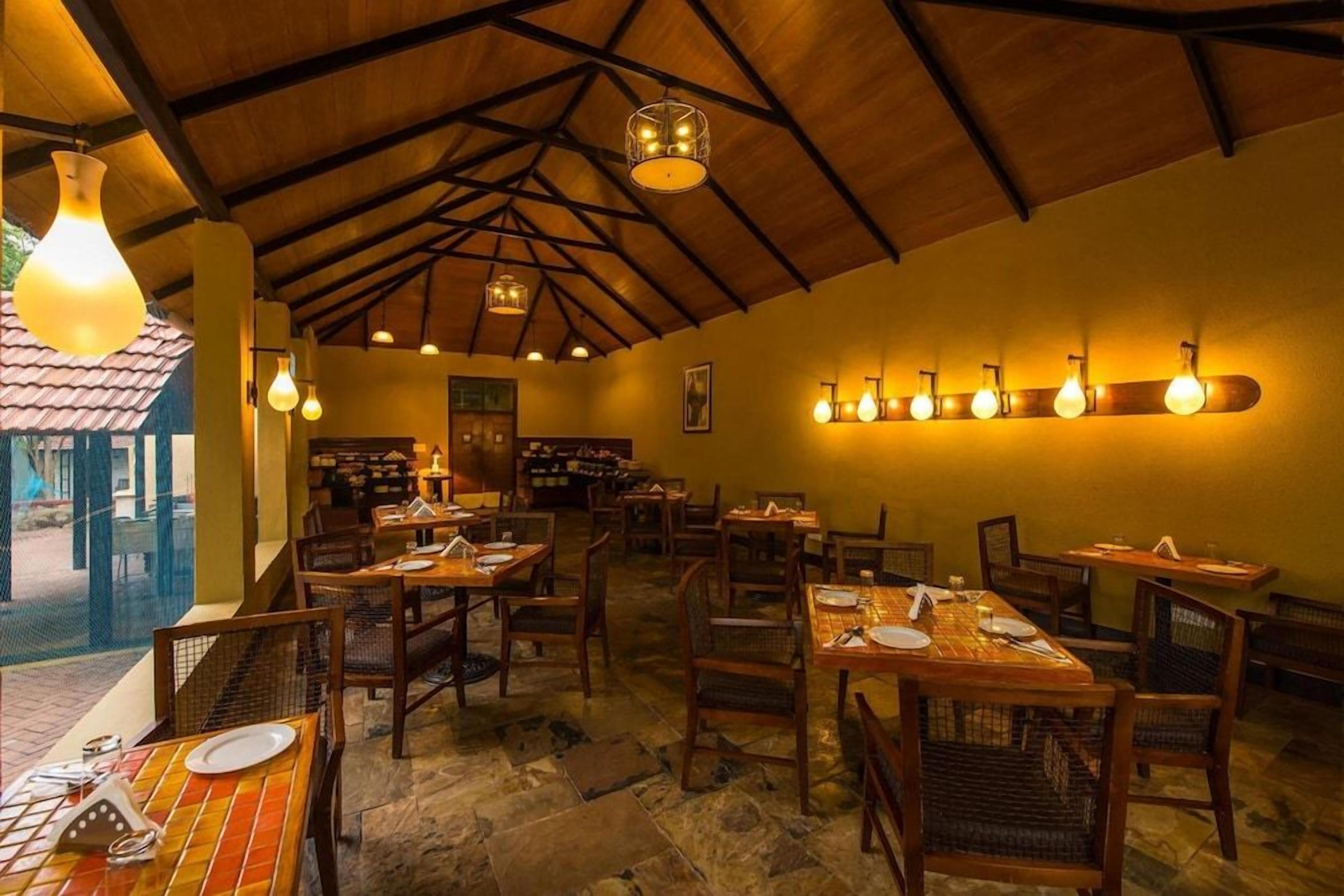 An indoor dining area with tables set for guests, wooden chairs, and hanging light fixtures.