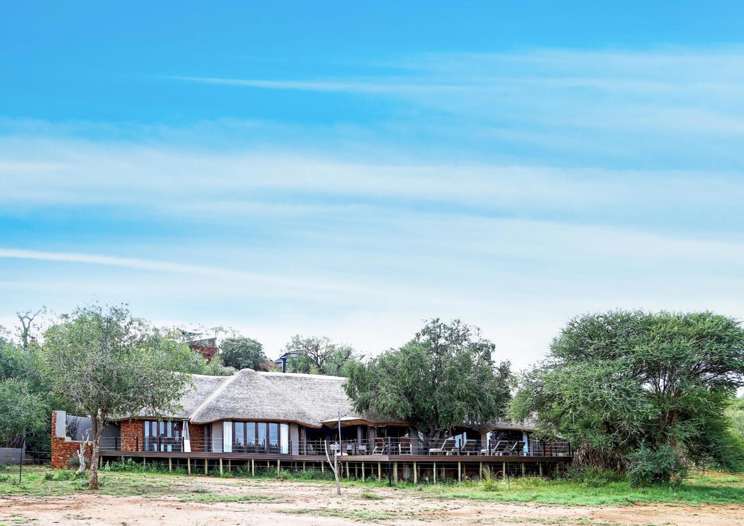 A thatched-roof building with a deck, surrounded by trees and vegetation.