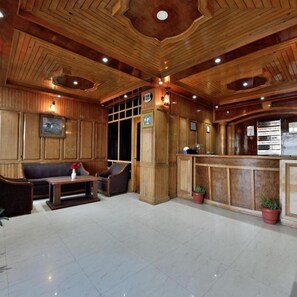 A lobby with wooden paneling, a reception desk, seating area, and a sign indicating a smoking area. - Galleu Hill Resorts (Theog)