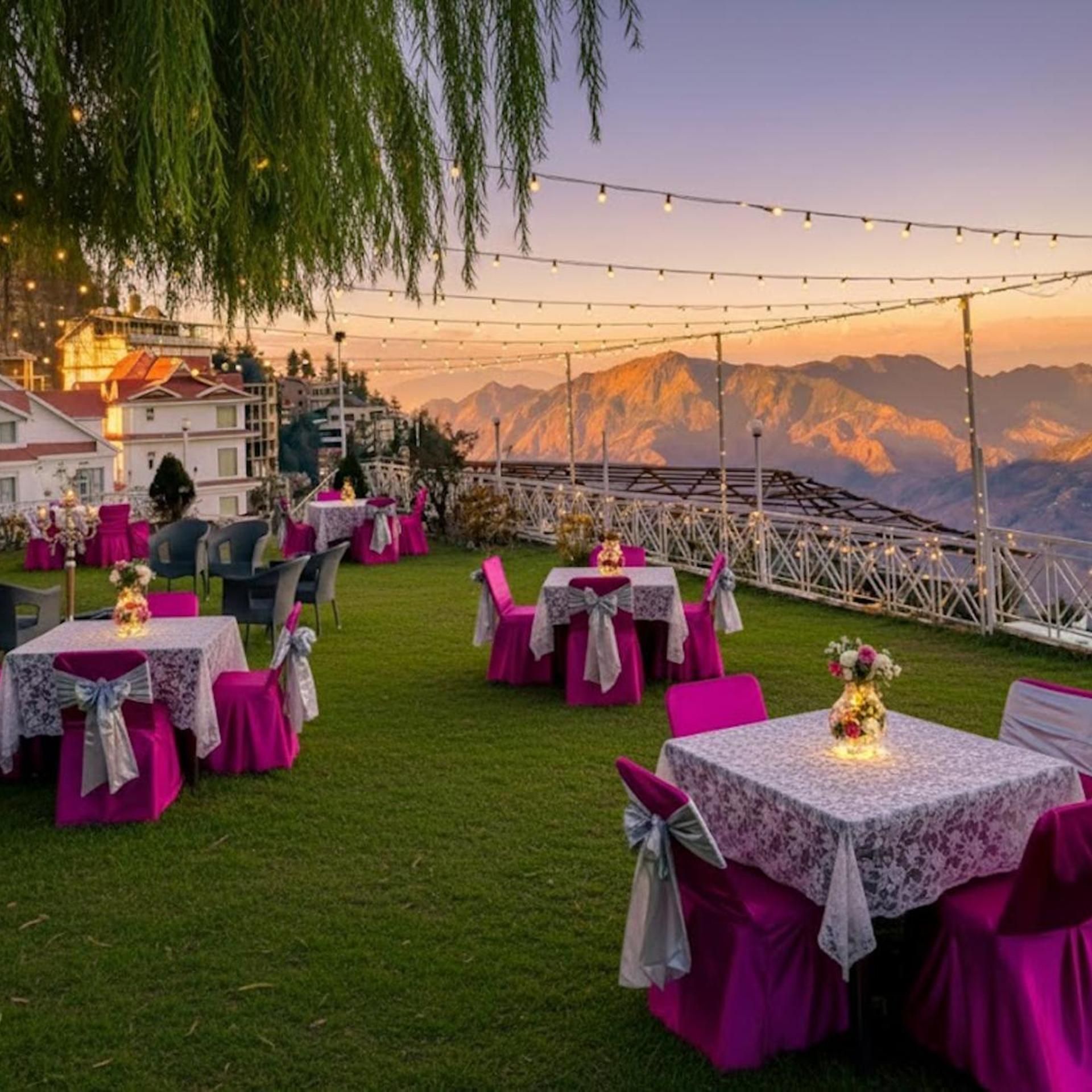 An outdoor dining area with tables and chairs, string lights, and a mountainous backdrop.