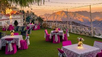 An outdoor dining area with tables and chairs, string lights, and a mountainous backdrop.