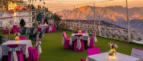 An outdoor dining area with tables and chairs, string lights, and a mountainous backdrop.