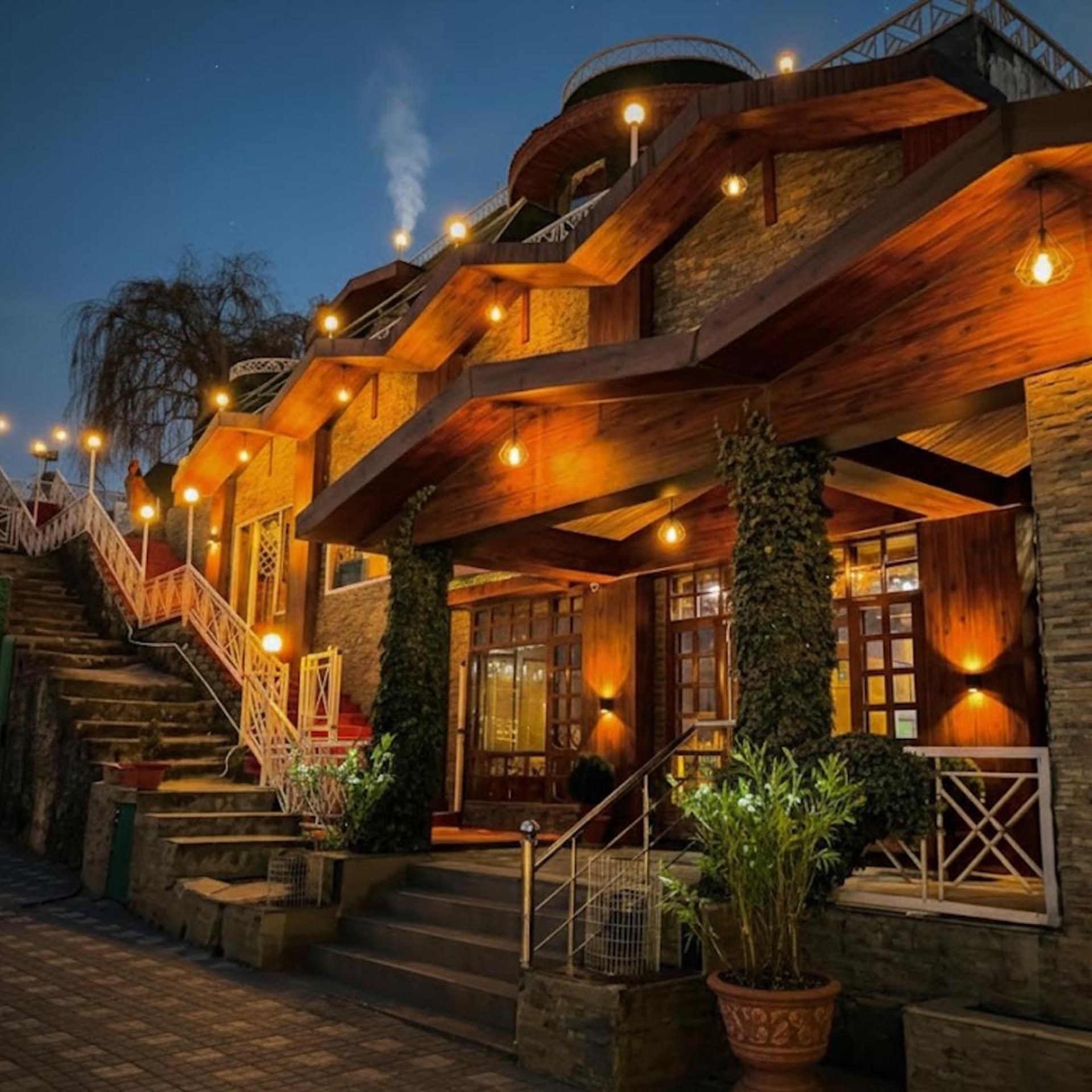 A multi-level wooden building with outdoor stairs and illuminated fixtures.