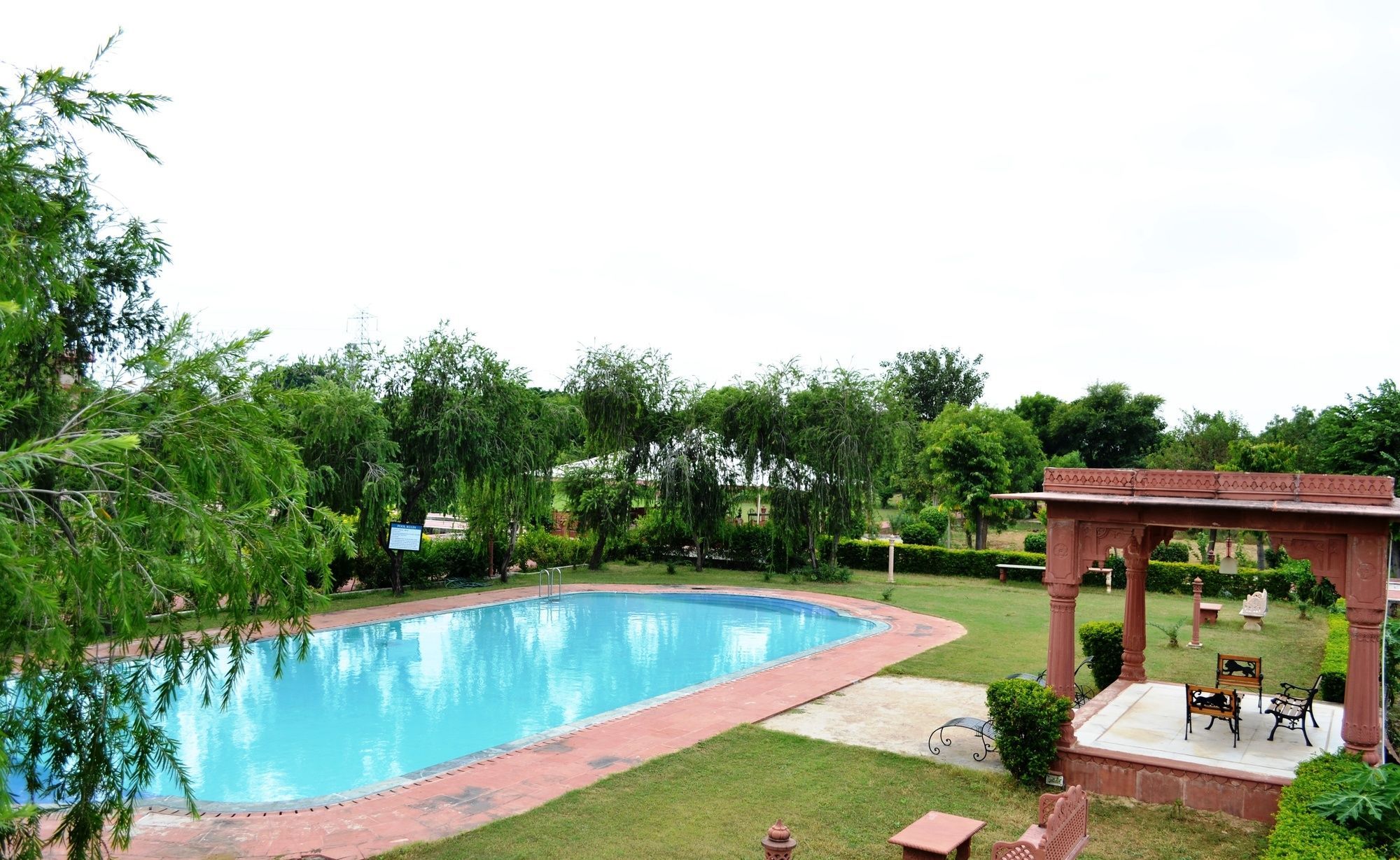 A swimming pool with a surrounding garden, a gazebo, and a bench area.