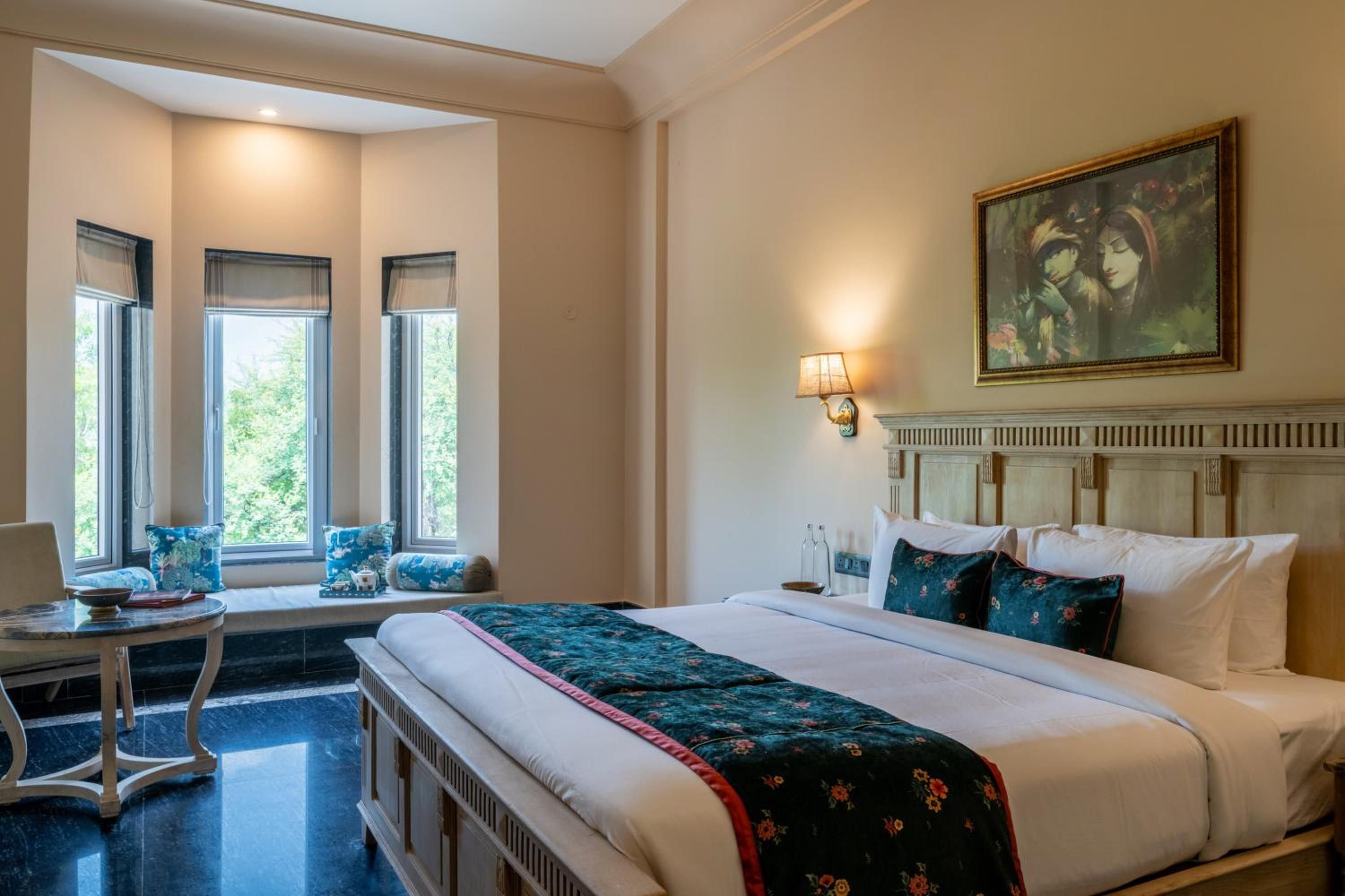 A hotel room with a large bed, a desk, and a window with a view of greenery.
