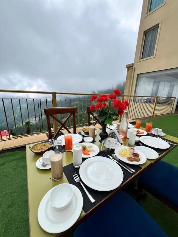 A dining table set with plates, cutlery, and beverages, overlooking a scenic view. - Kufri Holiday Resort (Theog)