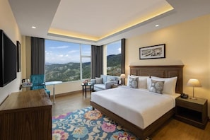 A hotel room with a large bed, a desk, a chair, and a view of the mountains. - Kufri Holiday Resort (Theog)