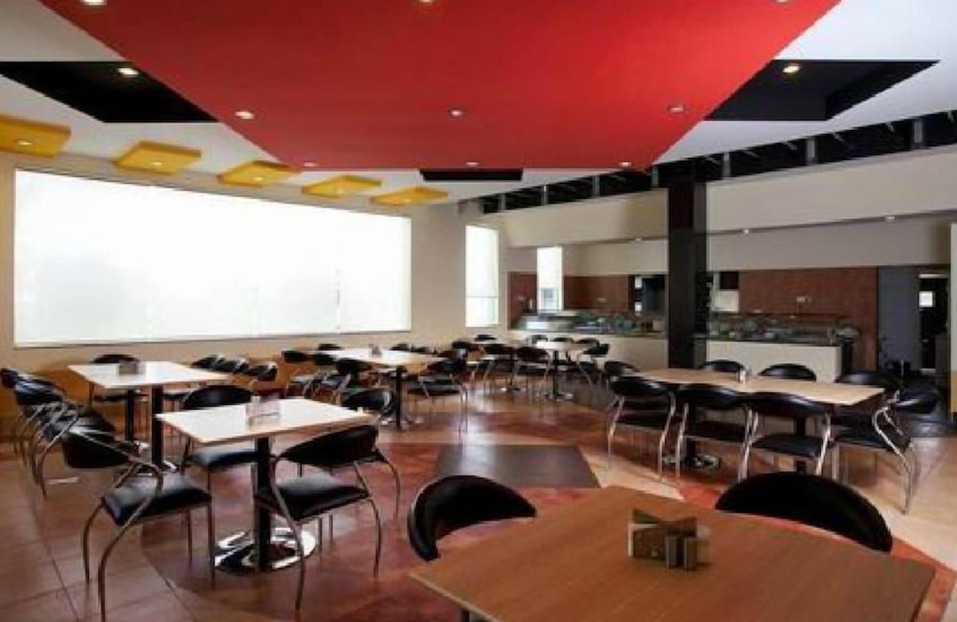 A modern conference room with tables and chairs, a large whiteboard, and a kitchen area.
