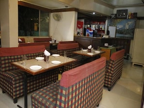 A restaurant with checkered booths and tables, a bar area, and a refrigerator in the background. - OYO Rooms Old Pune Bangalore Road Kolhapur (Kolhapur)