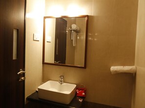 A bathroom with a white sink, a mirror, and a towel dispenser. - OYO Rooms Old Pune Bangalore Road Kolhapur (Kolhapur)