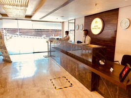 Zona de recepción de un hotel con un mostrador de mármol, un reloj y un letrero que dice 'Hotel Central Park New Delhi'.