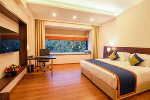 Una habitación de hotel con cama, escritorio, televisión y ventana con vista a árboles.
