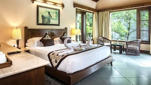 A hotel room with a large bed, a desk, a chair, and a view of greenery outside. - Aahana Resort and Spa- Jim Corbett (Ramnagar)