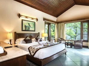 A hotel room with a large bed, a desk, a chair, and a view of greenery outside. - Aahana Resort and Spa- Jim Corbett (Ramnagar)