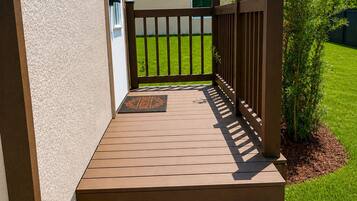 A wooden deck leading to a house with a gated entrance, a doormat, and a well-maintained lawn.