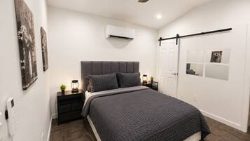 Ein modernes Schlafzimmer mit Bett, Nachttischen, Deckenventilator, Klimaanlage und Kunstwerken an den Wänden.