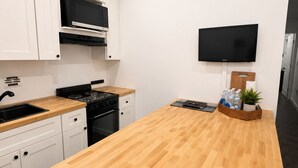 A modern kitchen with white cabinets, a wooden countertop, a stove, and a flat-screen TV mounted on the wall. - Modern Independent Tiny House (Lehigh Acres)